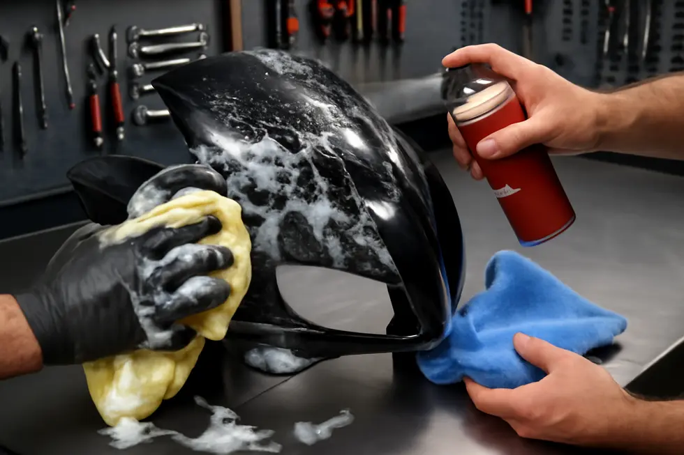 Technician thoroughly cleaning and preparing a scratched motorcycle fairing for repair.