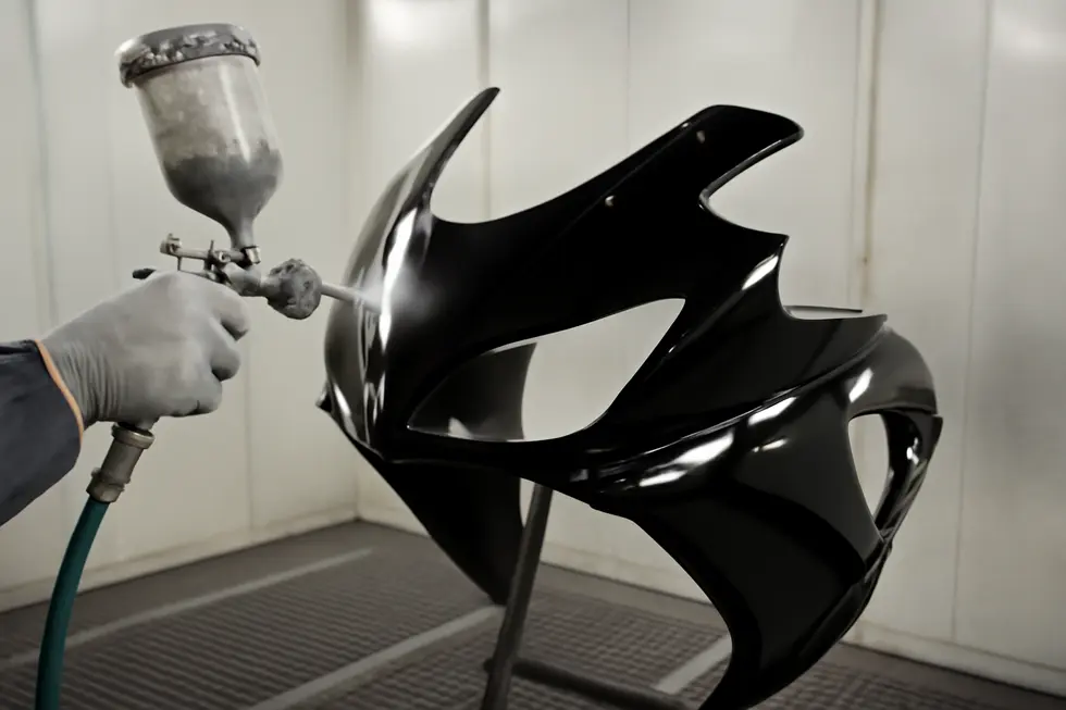 Mixing a two-part epoxy system for strong motorcycle fairing repairs in a professional garage setting.