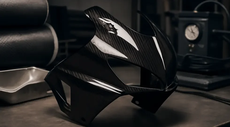 Finished carbon fiber motorcycle fairing displayed in a manufacturing environment highlighting advanced composite production.