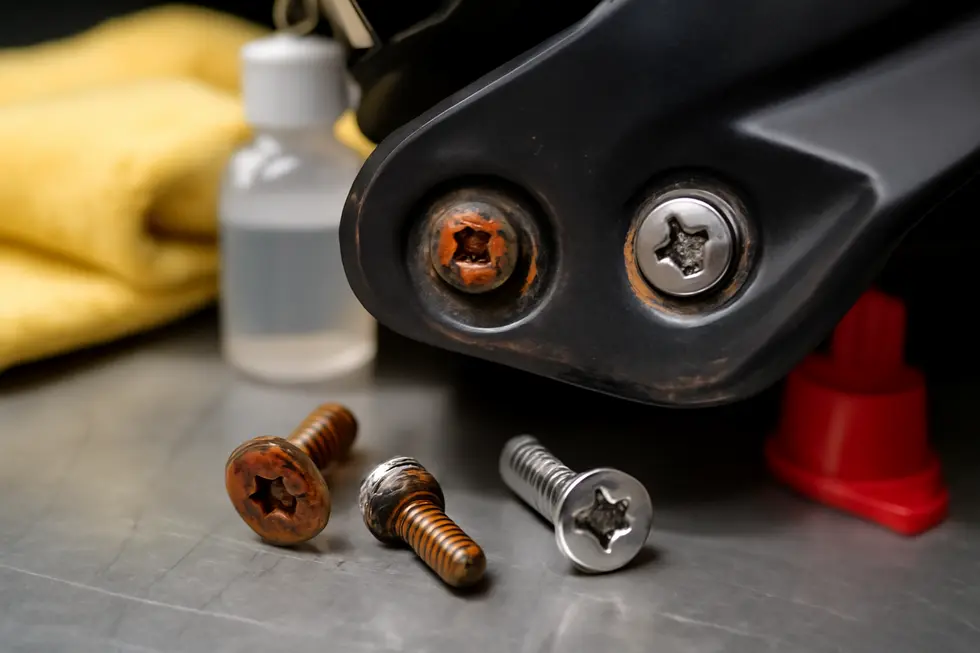 Worn and stripped motorcycle fairing screws contrasted with new stainless steel replacements, illustrating maintenance challenges.